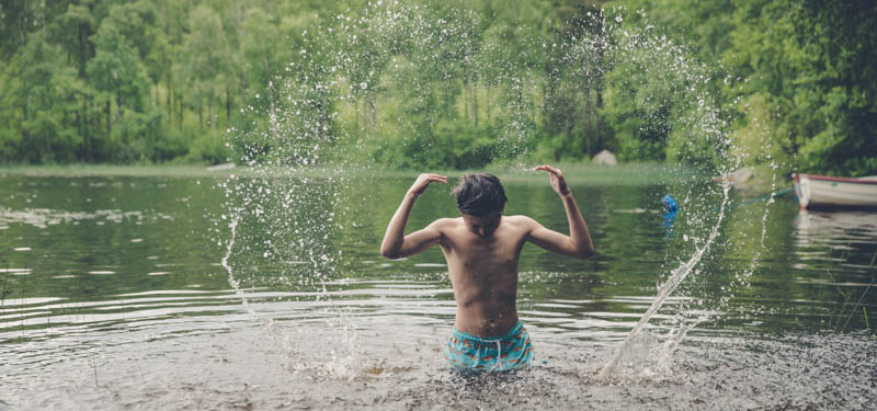 Ung kille badar i sjö.